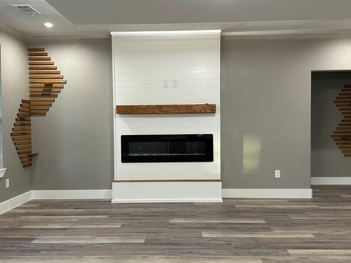 unfurnished living room featuring hardwood / wood-style floors, a large fireplace, and crown molding