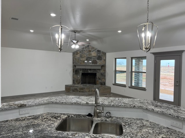 kitchen featuring pendant lighting, lofted ceiling, ceiling fan with notable chandelier, sink, and a fireplace