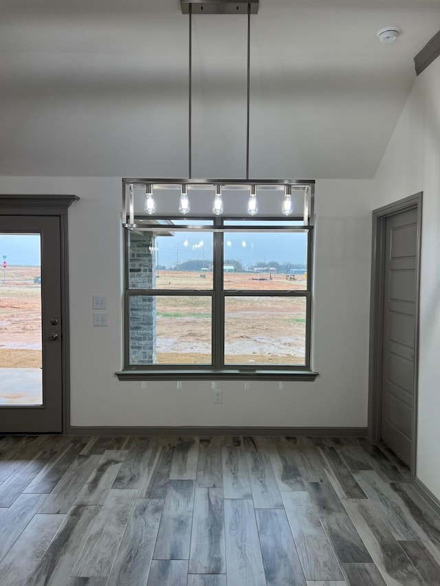 unfurnished dining area featuring wood-type flooring and vaulted ceiling