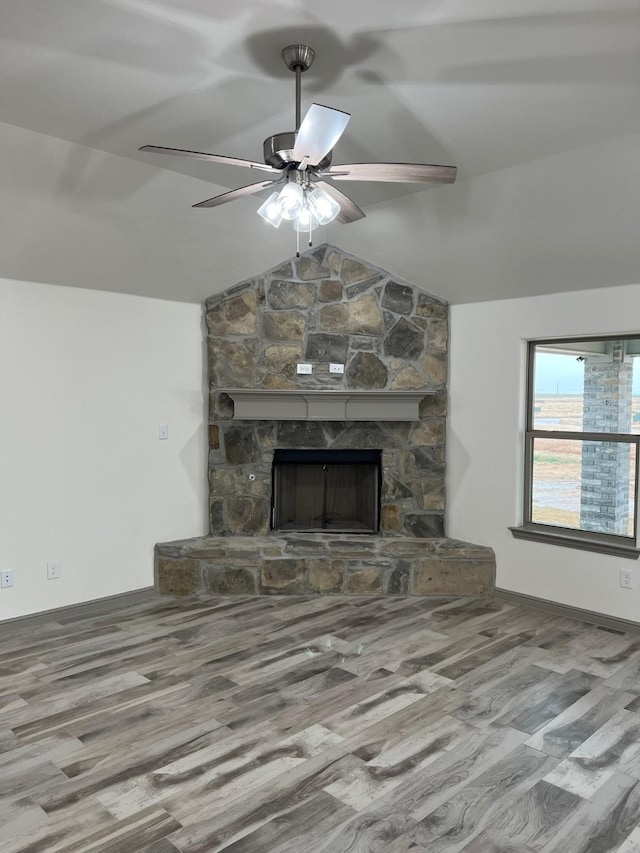 unfurnished living room with hardwood / wood-style flooring, ceiling fan, a stone fireplace, and lofted ceiling