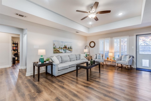 living room featuring dark hardwood / wood-style flooring, a tray ceiling, and ceiling fan