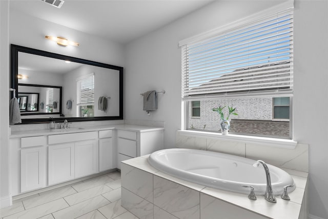 bathroom with a healthy amount of sunlight, tiled tub, and vanity