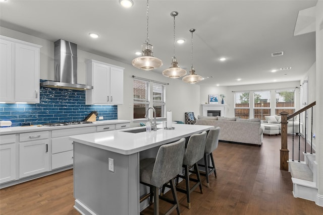 kitchen with white cabinetry, sink, wall chimney range hood, and an island with sink