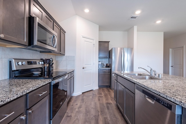 kitchen featuring sink, dark wood-type flooring, light stone counters, backsplash, and appliances with stainless steel finishes