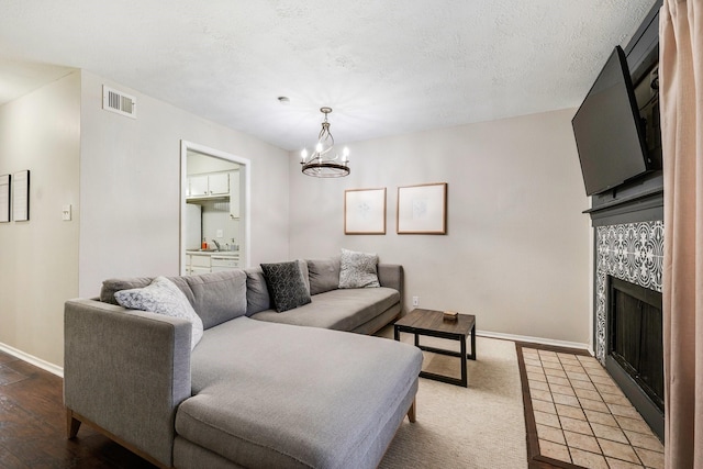 living room with a notable chandelier, a fireplace, wood-type flooring, and a textured ceiling