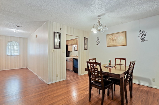 dining space with hardwood / wood-style floors, a textured ceiling, a notable chandelier, and wood walls