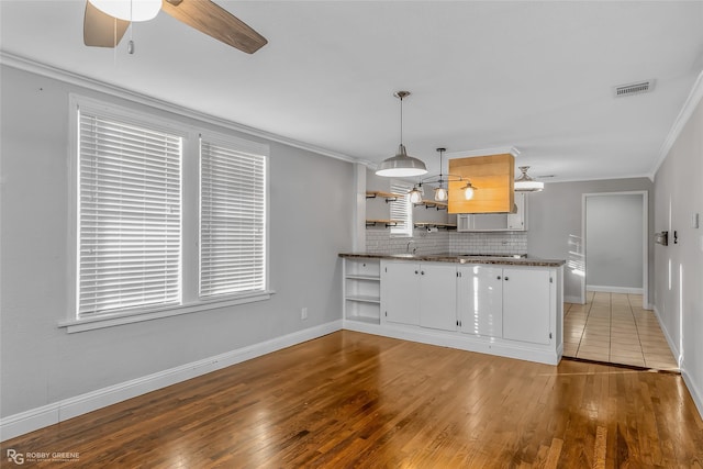 kitchen featuring hardwood / wood-style floors, white cabinets, decorative backsplash, hanging light fixtures, and ornamental molding