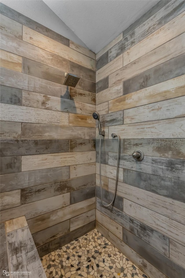 bathroom with lofted ceiling, wood walls, a textured ceiling, and tiled shower