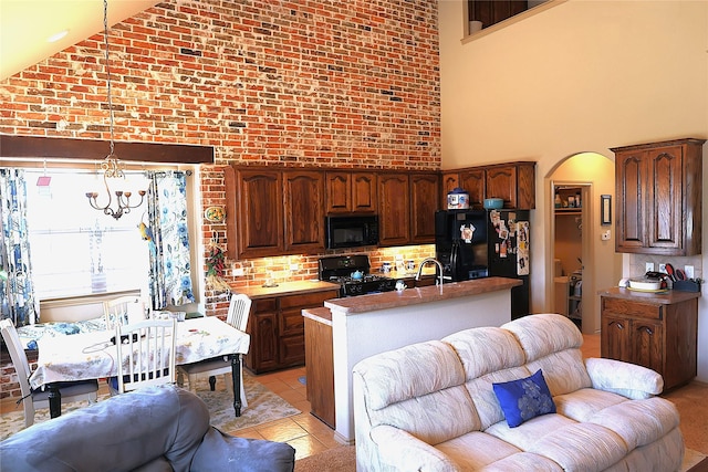 kitchen featuring high vaulted ceiling, light tile patterned floors, pendant lighting, brick wall, and black appliances