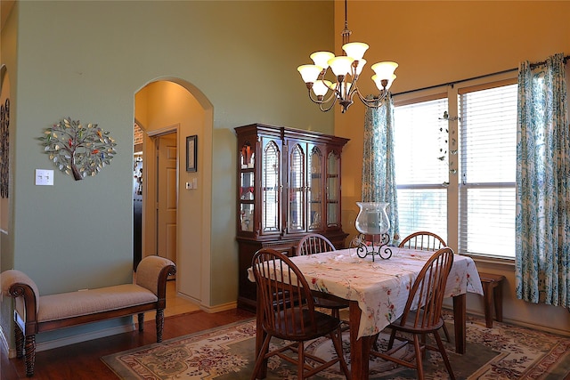 dining area featuring dark wood-type flooring, a notable chandelier, and a towering ceiling