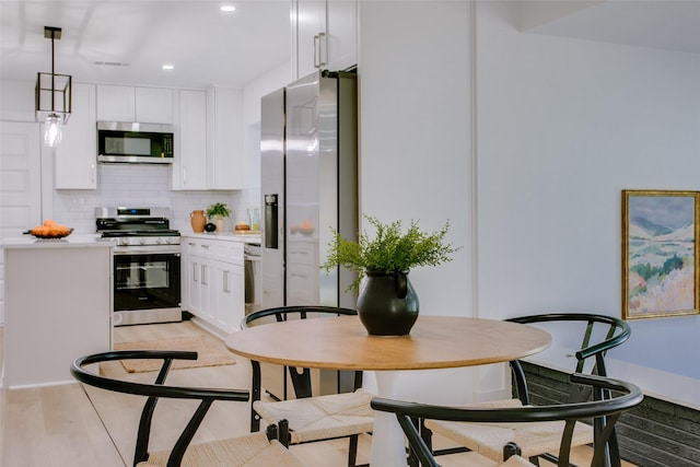 kitchen featuring white cabinets, decorative light fixtures, backsplash, and appliances with stainless steel finishes