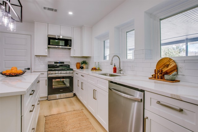 kitchen with sink, stainless steel appliances, light stone counters, backsplash, and white cabinets