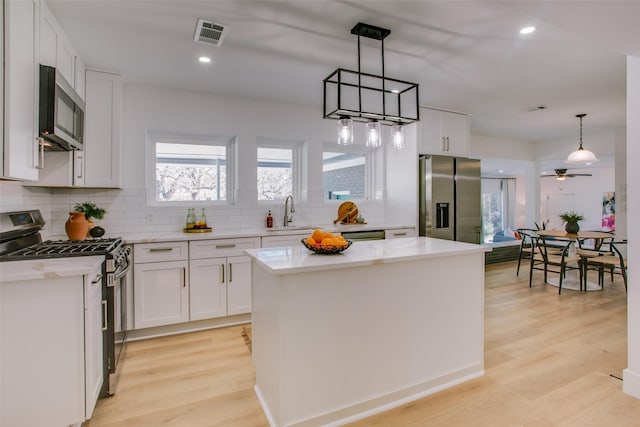 kitchen with white cabinets, decorative light fixtures, a center island, and stainless steel appliances