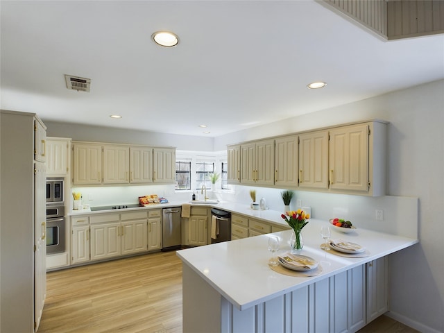 kitchen featuring stainless steel appliances, sink, light hardwood / wood-style floors, and kitchen peninsula