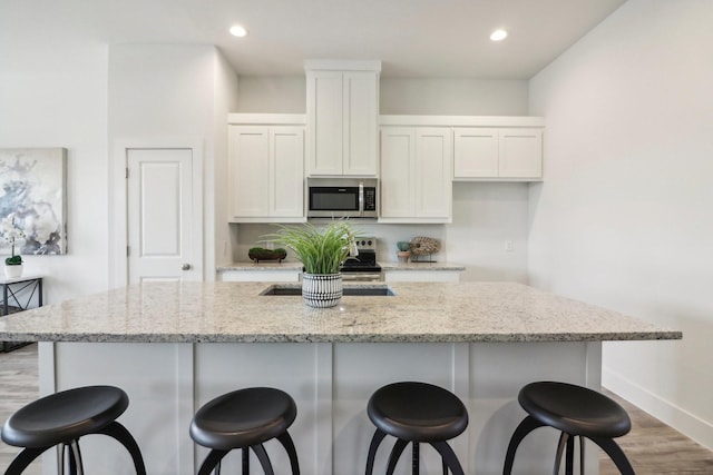 kitchen with appliances with stainless steel finishes, white cabinetry, an island with sink, a breakfast bar area, and light stone counters