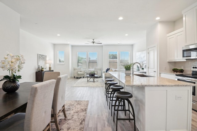 kitchen with sink, appliances with stainless steel finishes, white cabinetry, light stone counters, and a center island with sink