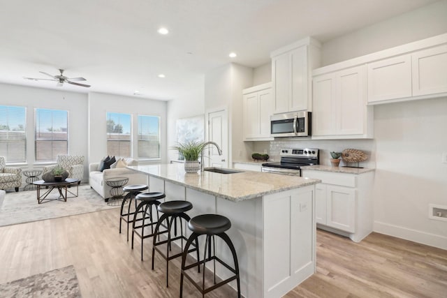 kitchen featuring sink, white cabinetry, appliances with stainless steel finishes, a kitchen breakfast bar, and an island with sink