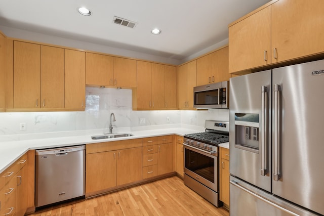 kitchen featuring appliances with stainless steel finishes, light brown cabinetry, sink, decorative backsplash, and light hardwood / wood-style floors