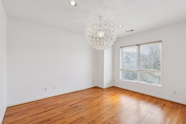 empty room featuring a notable chandelier and wood-type flooring