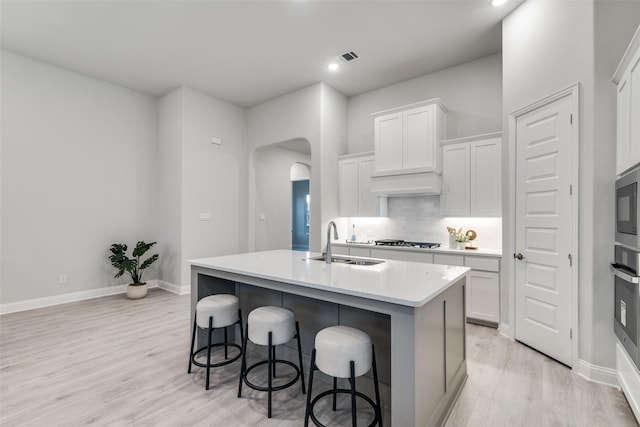 kitchen with sink, tasteful backsplash, white cabinetry, and an island with sink