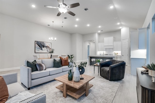 living room featuring ceiling fan with notable chandelier and light wood-type flooring