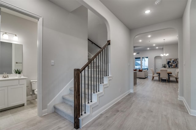 staircase featuring wood-type flooring, ceiling fan with notable chandelier, and sink