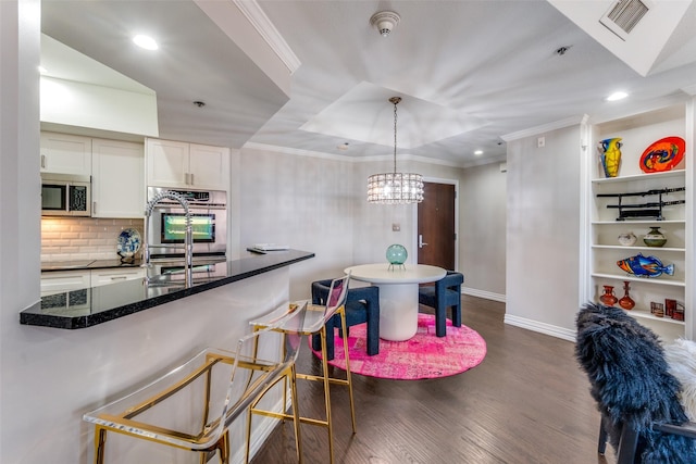 kitchen with appliances with stainless steel finishes, dark hardwood / wood-style flooring, a raised ceiling, white cabinetry, and hanging light fixtures