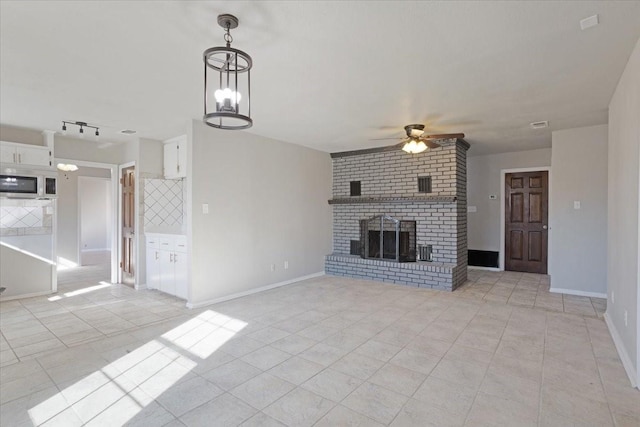 unfurnished living room featuring ceiling fan with notable chandelier, light tile patterned flooring, and a brick fireplace