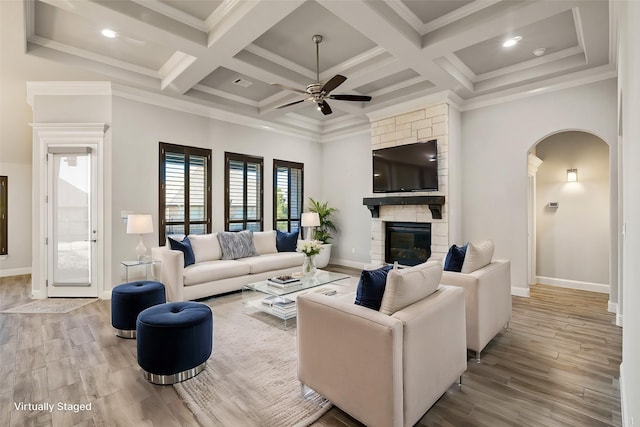 living room featuring light hardwood / wood-style floors, ceiling fan, ornamental molding, and a stone fireplace