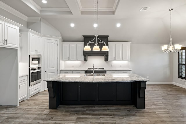 kitchen featuring white cabinets, an island with sink, light stone counters, and stainless steel appliances