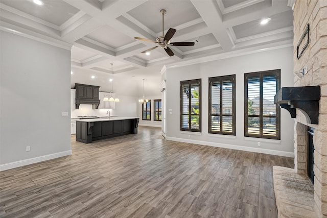 unfurnished living room with a stone fireplace, plenty of natural light, wood-type flooring, crown molding, and ceiling fan with notable chandelier