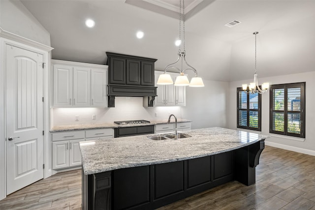 kitchen featuring vaulted ceiling, sink, white cabinets, and an island with sink