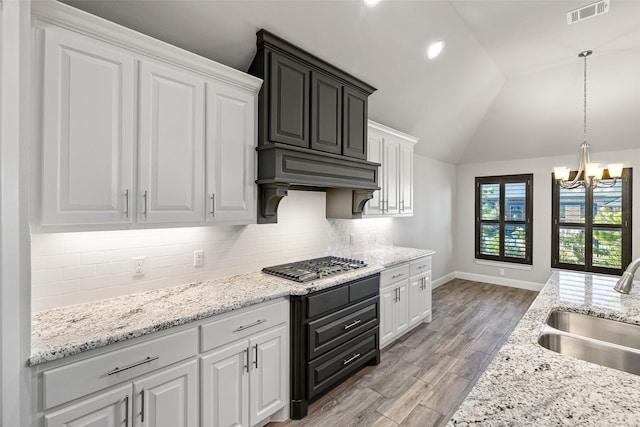 kitchen with stainless steel gas stovetop, an inviting chandelier, lofted ceiling, white cabinets, and sink