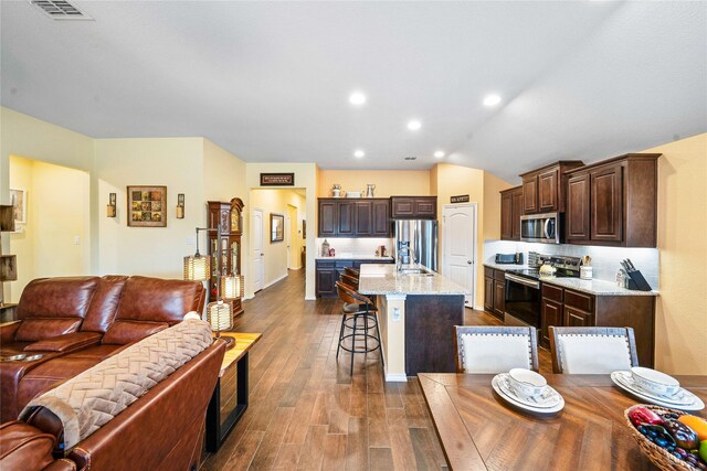 kitchen with sink, stainless steel appliances, dark hardwood / wood-style floors, decorative backsplash, and a center island with sink