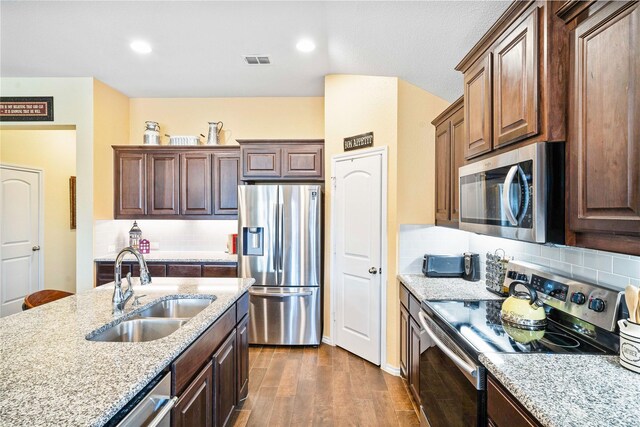 kitchen featuring sink, stainless steel appliances, light stone counters, dark brown cabinets, and a center island with sink