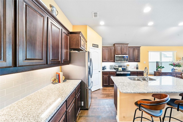 kitchen featuring lofted ceiling, a center island with sink, a breakfast bar area, ceiling fan, and stainless steel appliances