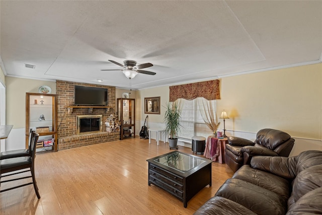 living room with hardwood / wood-style flooring, a brick fireplace, ceiling fan, a textured ceiling, and ornamental molding