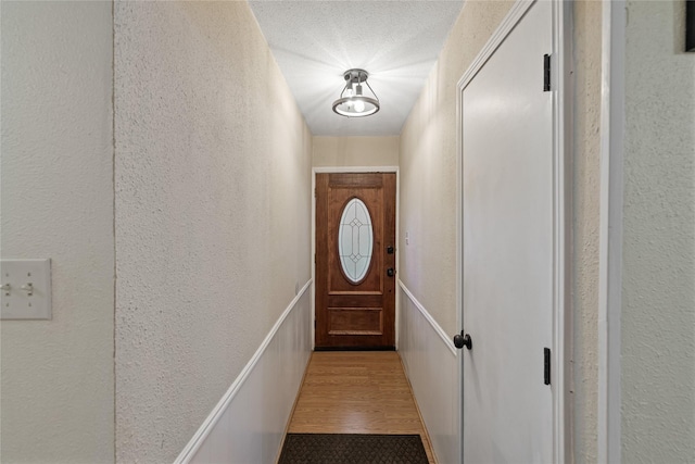 doorway to outside with a textured ceiling and light hardwood / wood-style flooring