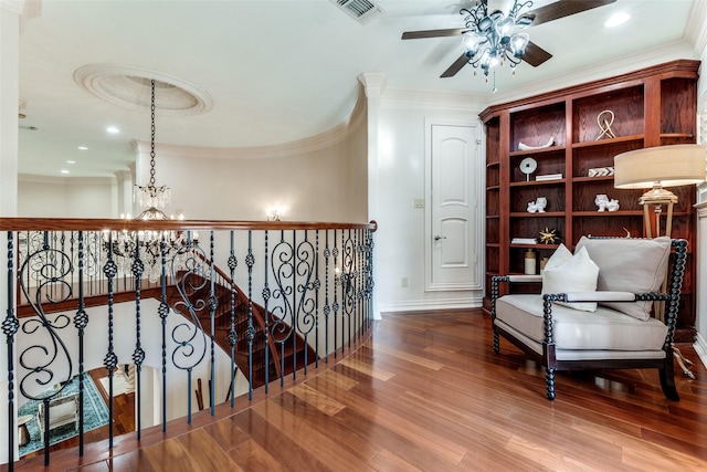 living area with ornamental molding, wood-type flooring, and ceiling fan with notable chandelier