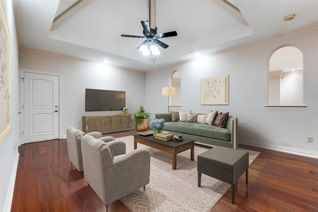 living room featuring dark wood-type flooring, ceiling fan, crown molding, and a raised ceiling