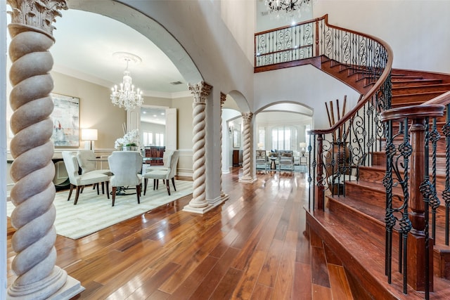 entrance foyer with crown molding, wood-type flooring, a healthy amount of sunlight, a chandelier, and ornate columns