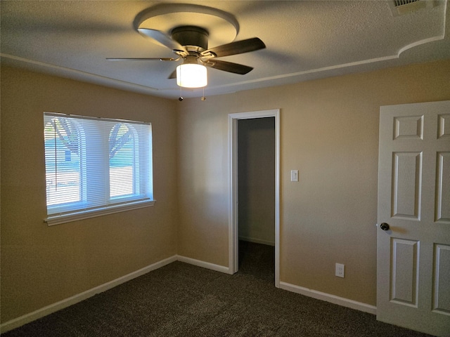 unfurnished bedroom with a walk in closet, ceiling fan, and dark carpet