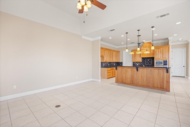 kitchen featuring backsplash, stainless steel microwave, ornamental molding, a kitchen island, and decorative light fixtures