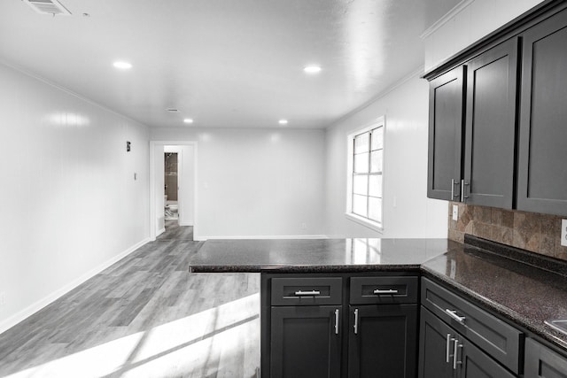 kitchen with kitchen peninsula, dark stone countertops, light hardwood / wood-style floors, decorative backsplash, and ornamental molding