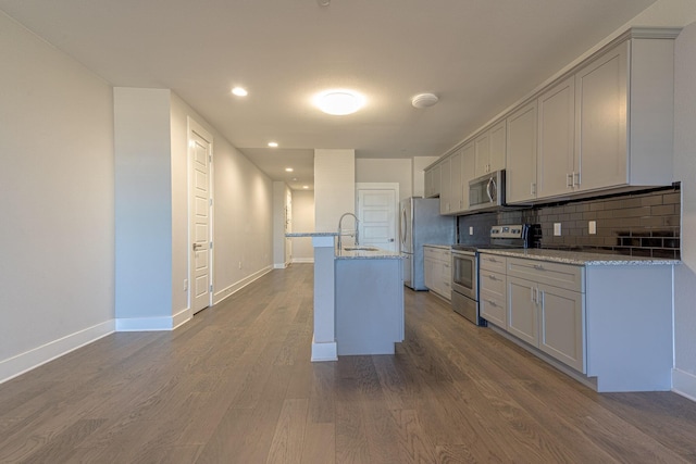 kitchen featuring sink, an island with sink, tasteful backsplash, light stone counters, and stainless steel appliances