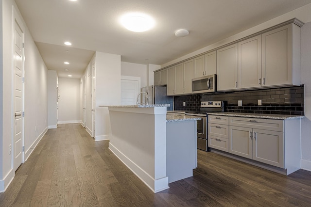 kitchen with light stone countertops, appliances with stainless steel finishes, decorative backsplash, gray cabinetry, and a kitchen island with sink