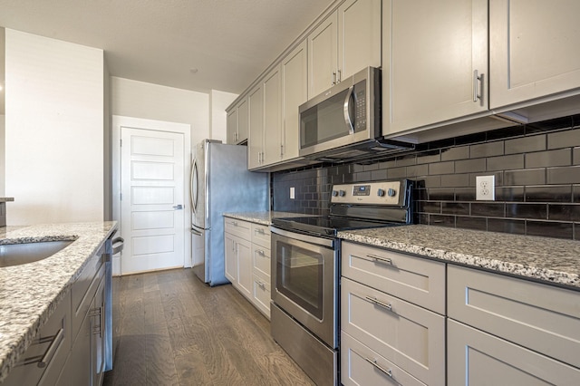 kitchen with sink, dark wood-type flooring, light stone counters, decorative backsplash, and appliances with stainless steel finishes