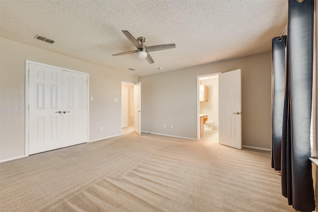 unfurnished bedroom with light carpet, a textured ceiling, ceiling fan, connected bathroom, and a closet