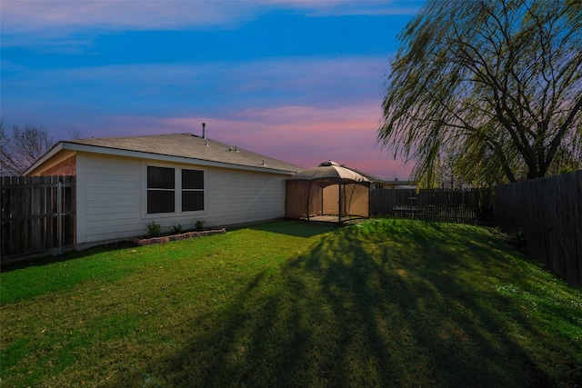 back house at dusk with a gazebo and a yard