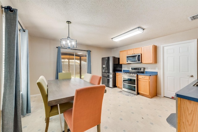 kitchen featuring a notable chandelier, a textured ceiling, decorative light fixtures, light brown cabinetry, and appliances with stainless steel finishes